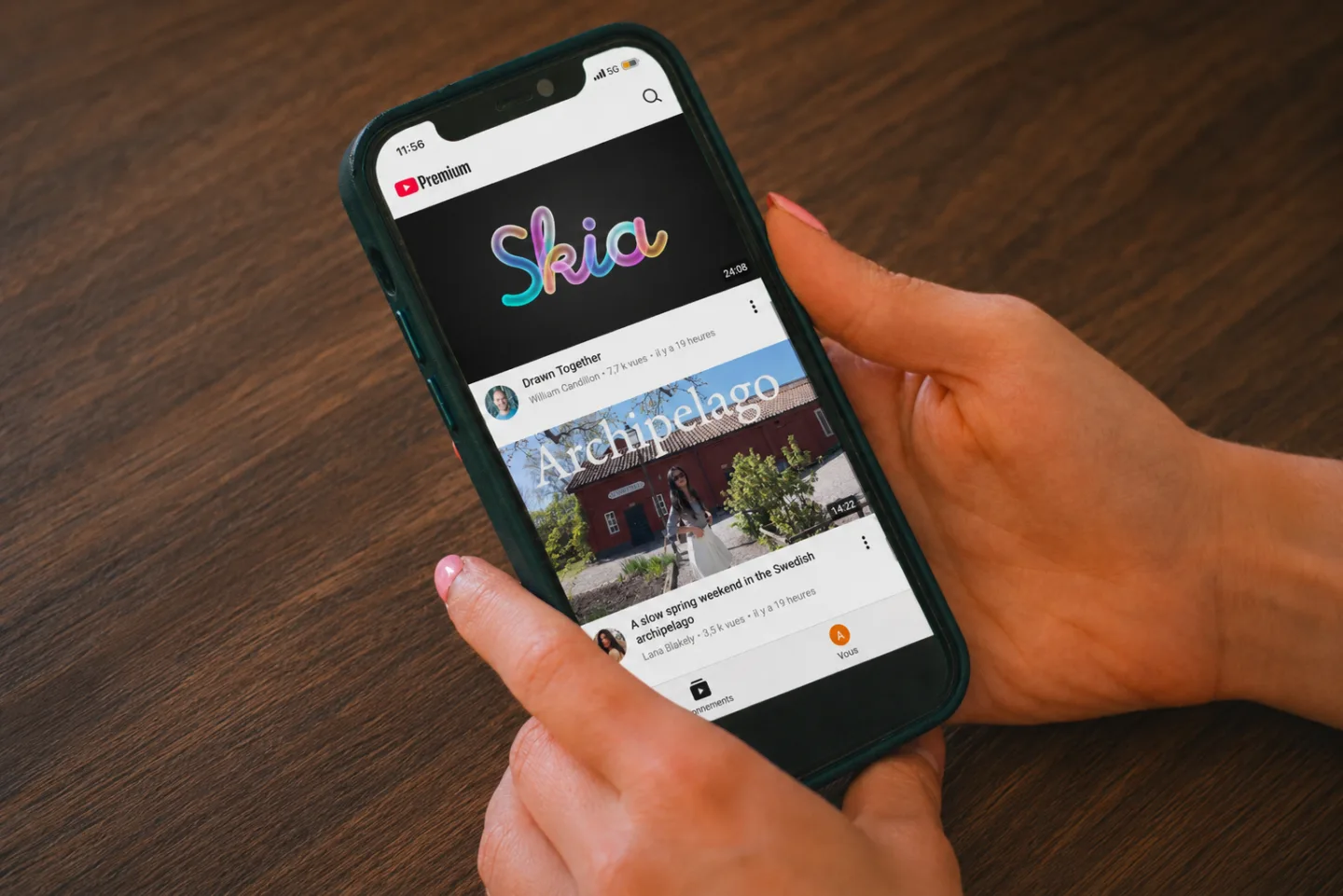 Hands holding an iPhone showing the YouTube mobile app with no Shorts tab in the bottom navigation — only Subscriptions and You — after Nope is enabled.